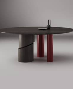 Table Ishikawa ronde en frêne teinté tabac, avec un grand pied à découpe diagonale et deux petits pieds Rosso brillant.