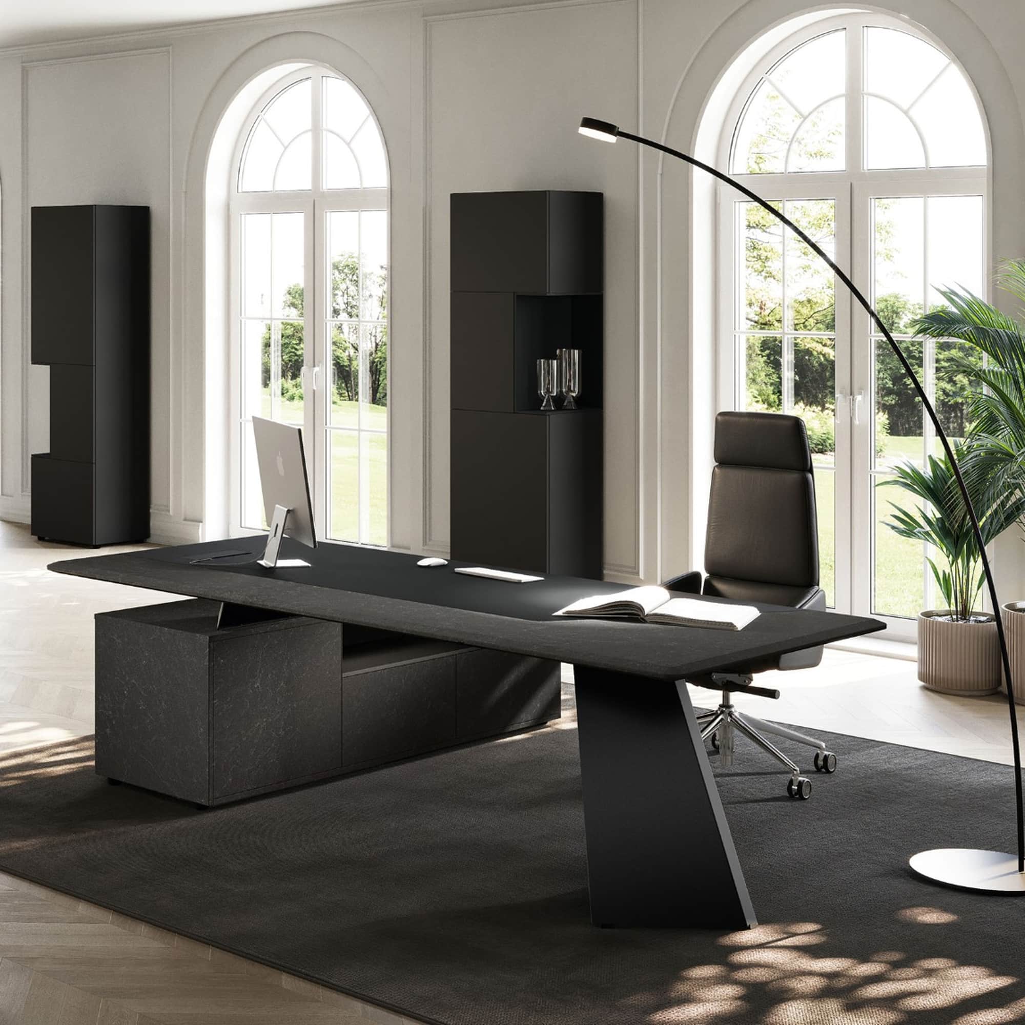 Angled view of the black MONOLITH desk with supporting side storage and a V-shaped metal leg.